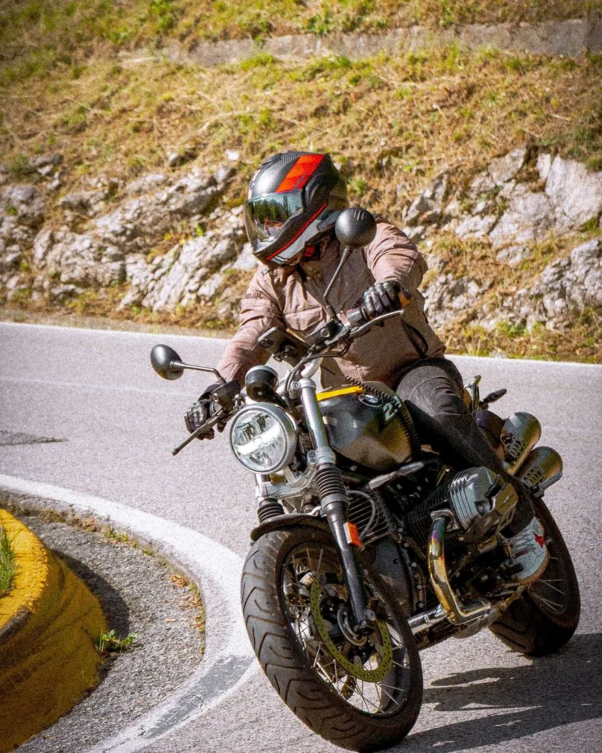 Benito in moto in una curva di montagna, con casco e giacca